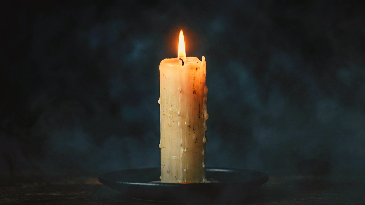 Obrazek ukazuje zapaloną, białą świecę.