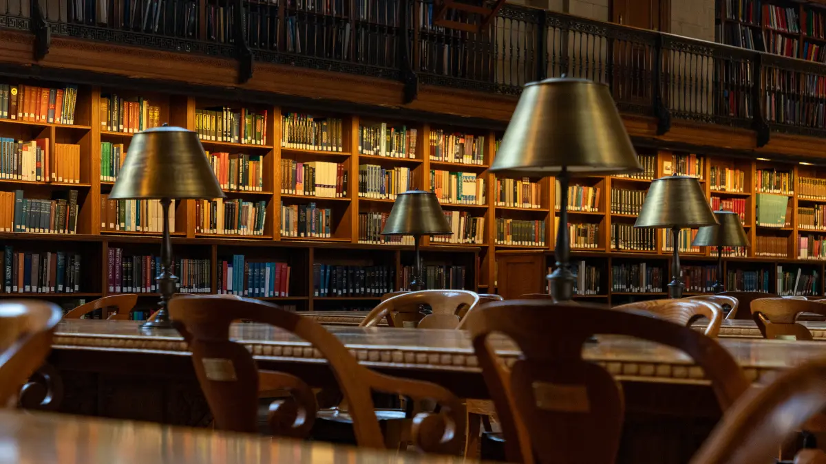 Obrazek przedstawia wnętrze starej biblioteki, na pierwszym planie stół, na drugim regały z książkami.
